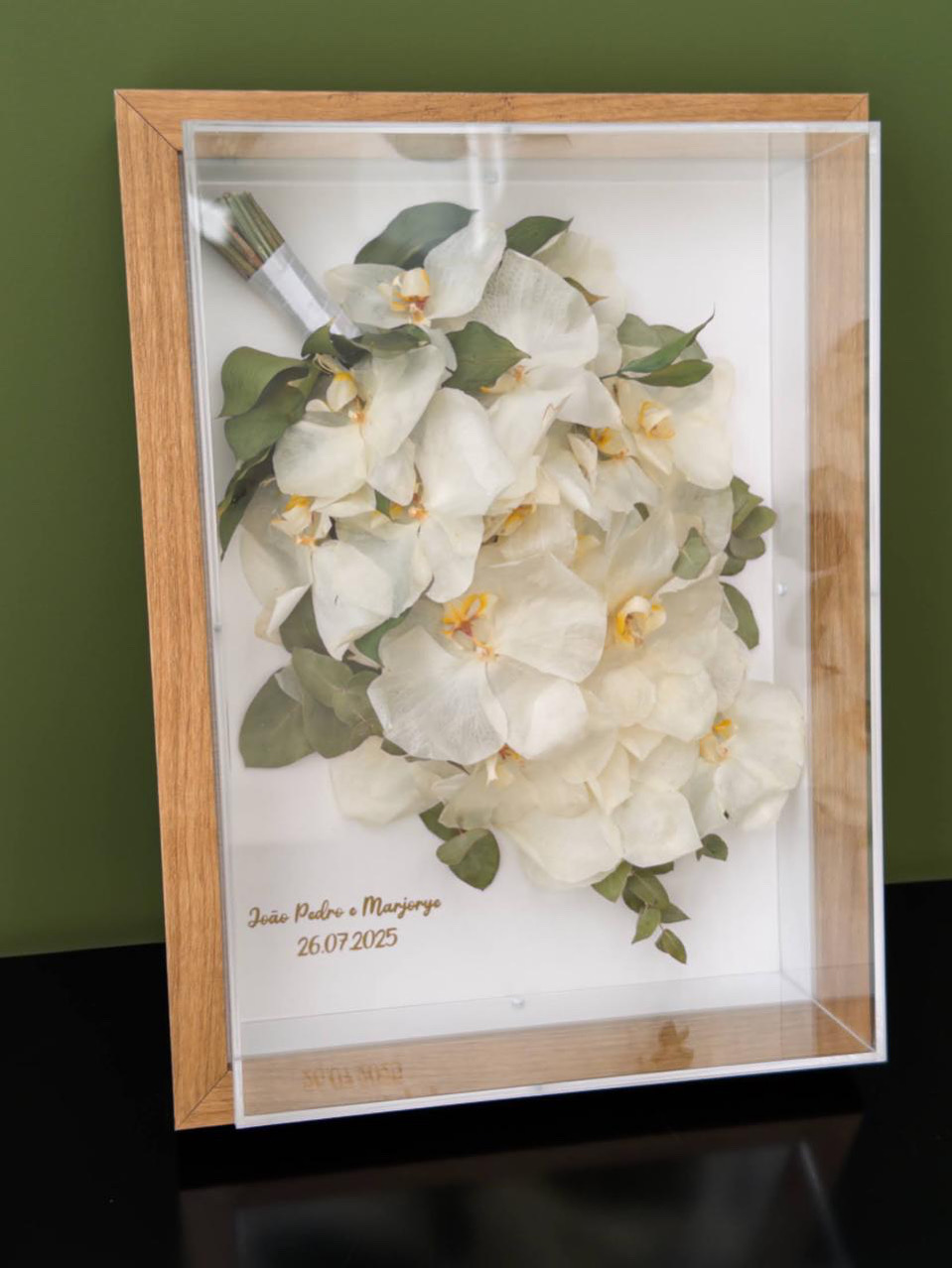 Orquídeas brancas e folhagens preservadas em quadro com moldura de madeira